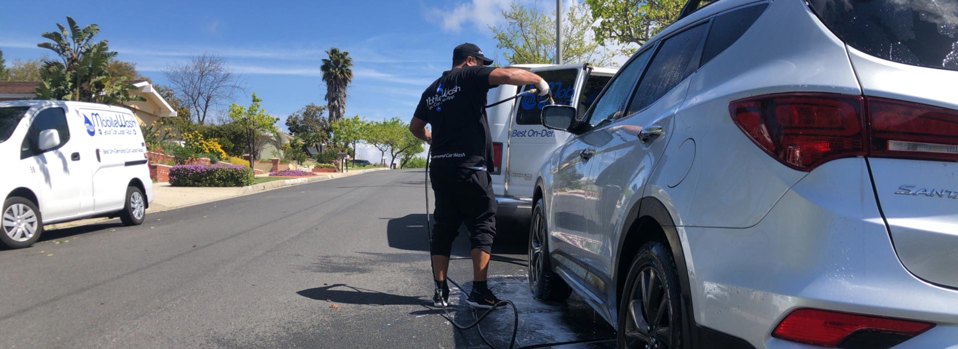 MobileWash washer sprays soap on a white SUV for a car cleaning.