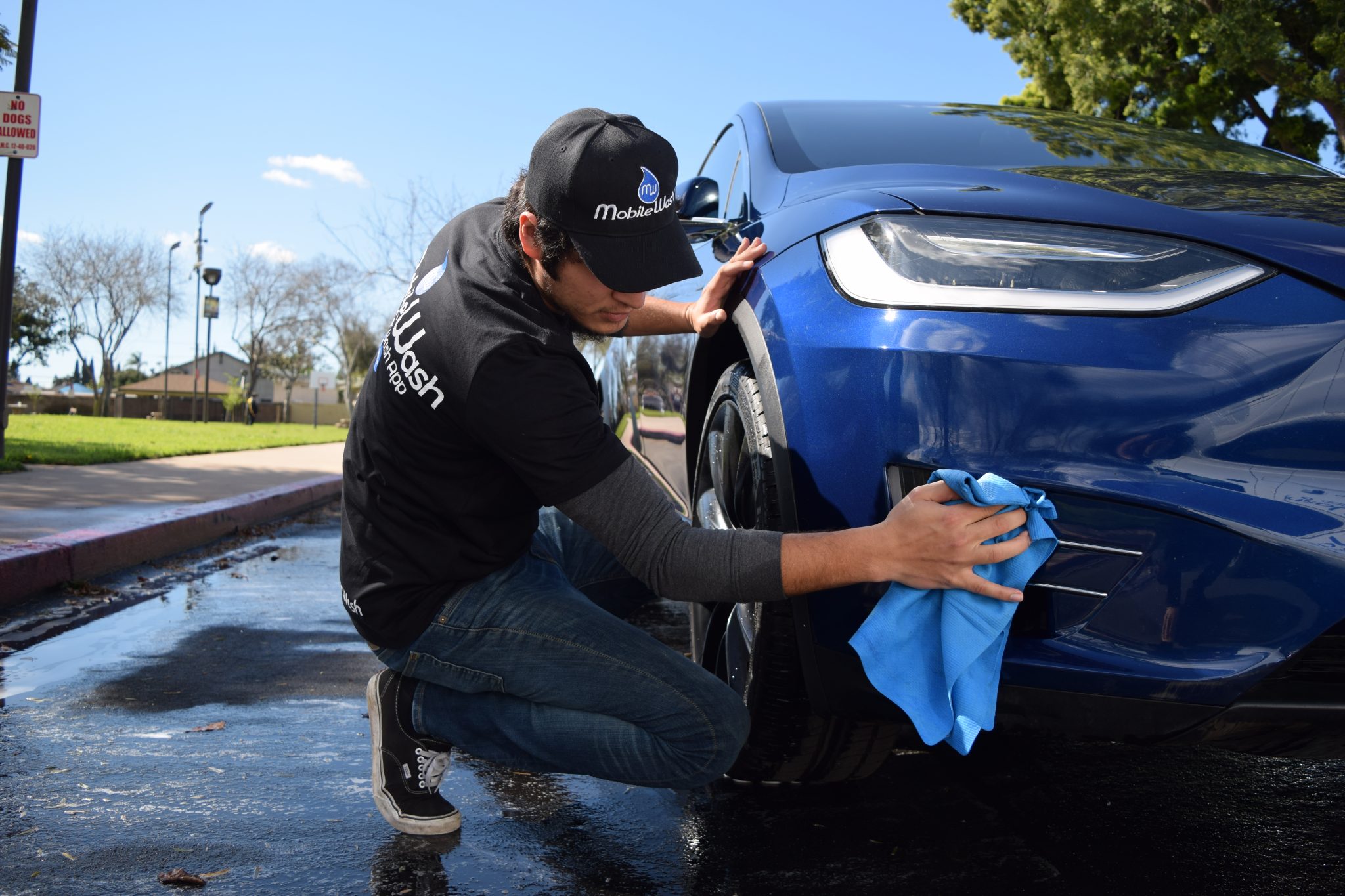 MobileWash washer does a hand wash on the front of a blue car for a mobile car wash..