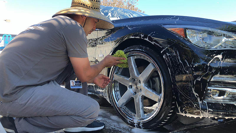 A MobileWash washer doing a tire-dressing for a black BMW for a car cleaning and mobile car detailing service.